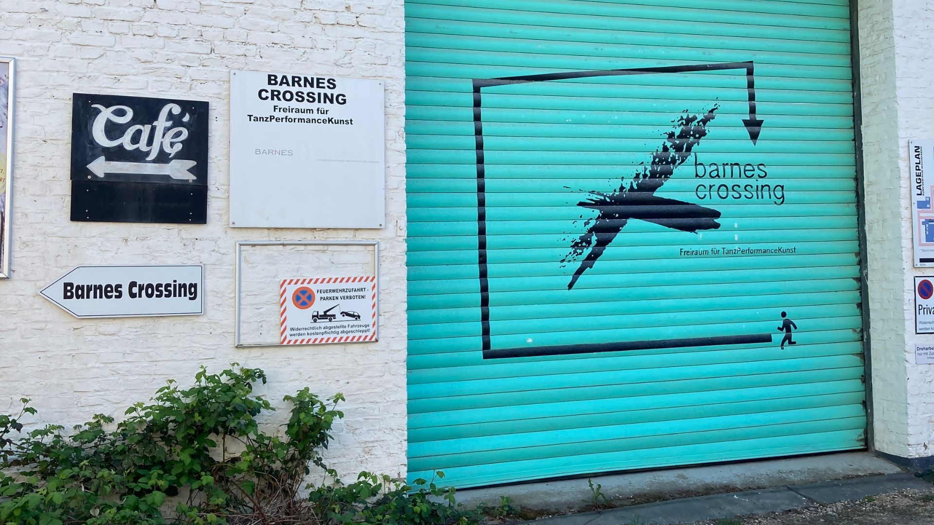 Türkisfarbenes Rolltor mit Barnes-Crossing-Logo und Wegweisern auf dem Gelände des Kunstzentrums Wachsfabrik.