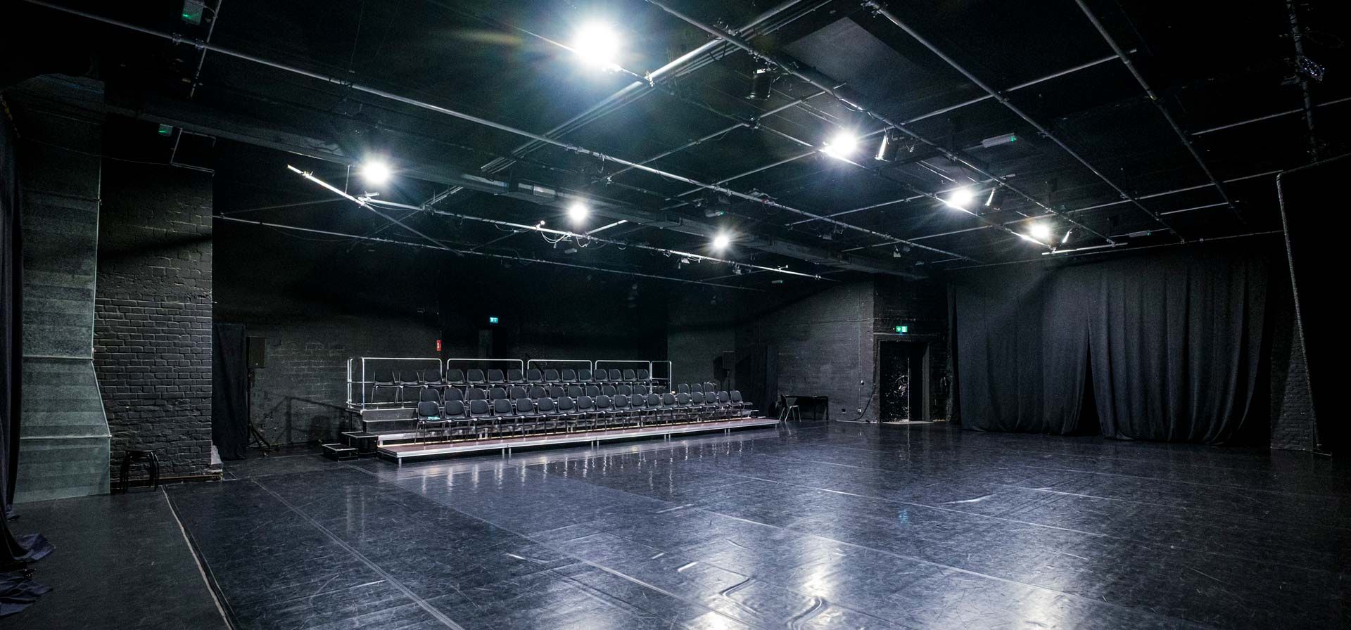 Studio 1 / Black Box bei Barnes Crossing mit schwarzem Tanzboden, Zuschauertribüne, Stuhlreihen und Bühnentechnik (u.a. Licht).
