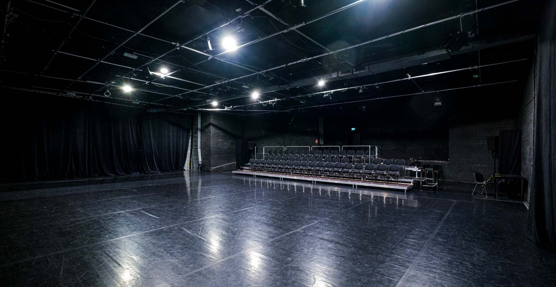 Studio 1 / Black Box bei Barnes Crossing mit schwarzem Tanzboden, Zuschauertribüne, Stuhlreihen und Bühnentechnik.