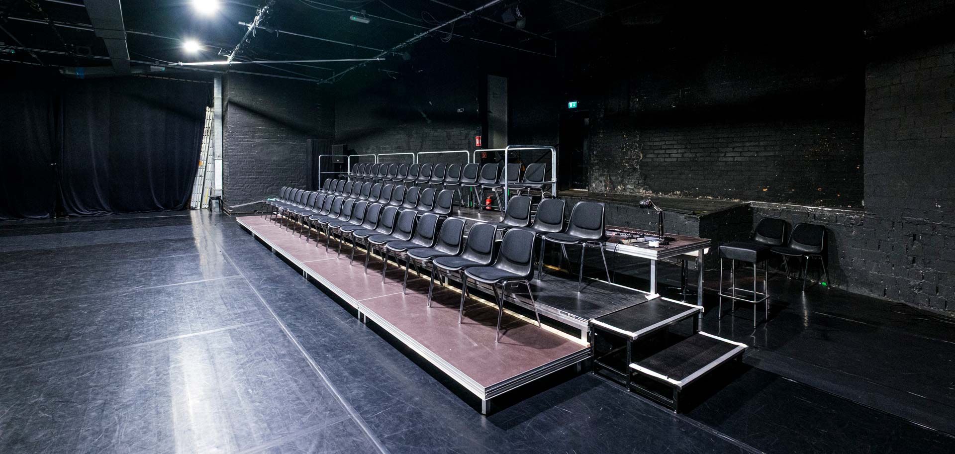 Studio 1 / Black Box bei Barnes Crossing mit Fokus auf die Zuschauertribüne mit Stuhlreihen (rechts im Bild). Links ist etwas schwarzer Tanzboden zu sehen.