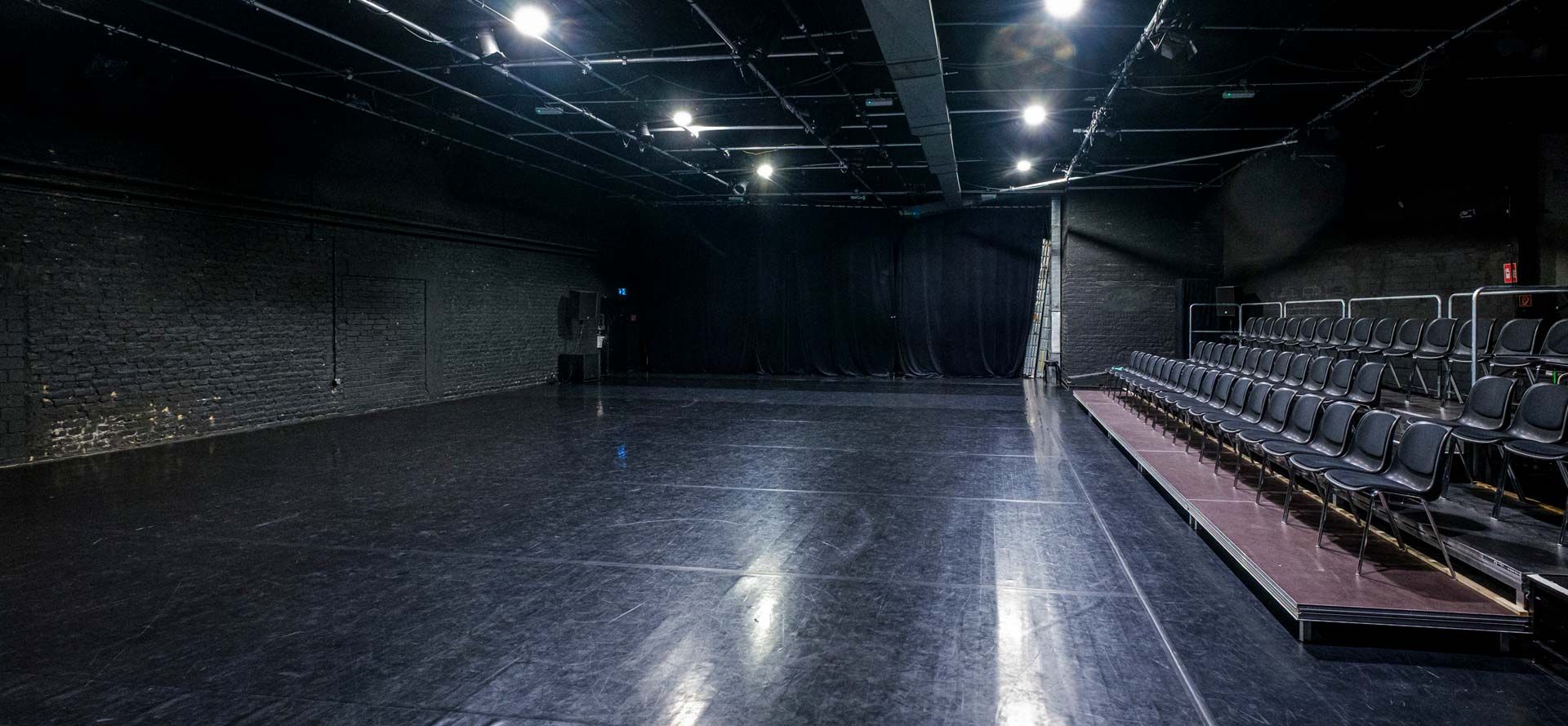 Studio 1 / Black Box bei Barnes Crossing mit schwarzem Tanzboden, Zuschauertribüne, Stuhlreihen (rechts) und Bühnentechnik.