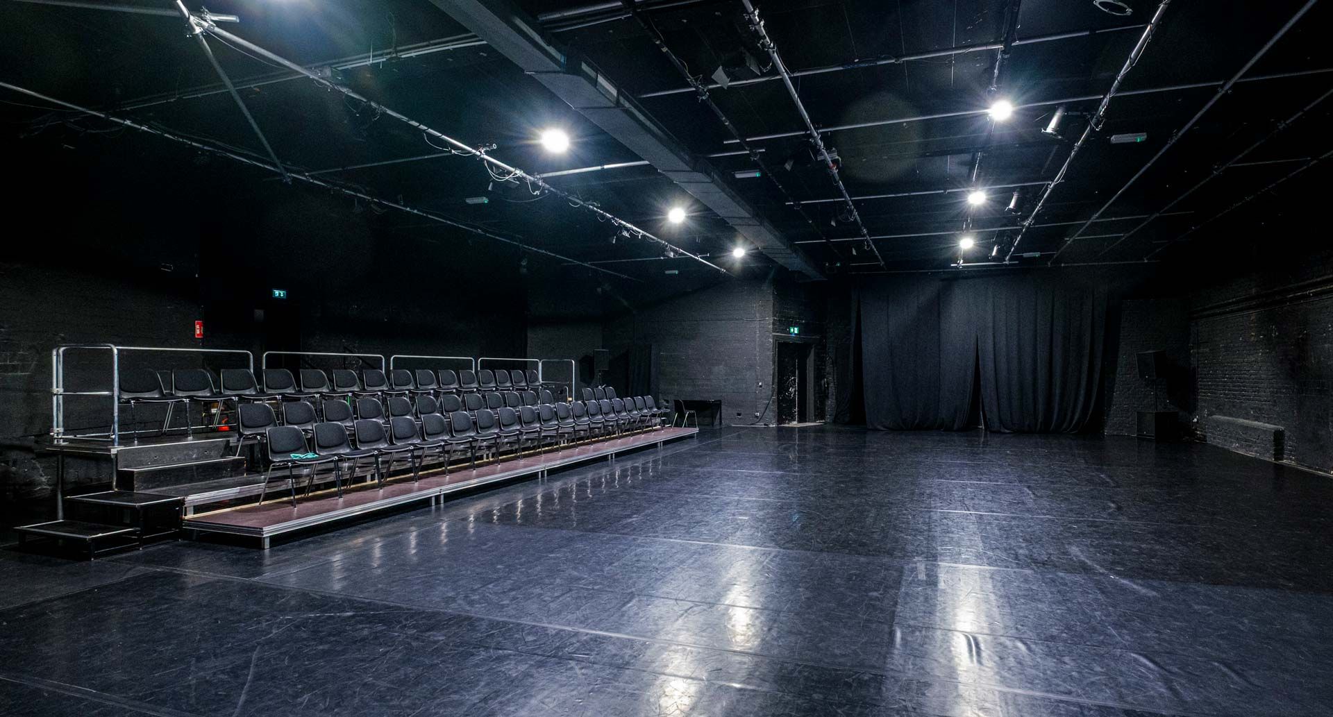Studio 1 / Black Box bei Barnes Crossing mit schwarzem Tanzboden, Zuschauertribüne, Stuhlreihen und Bühnentechnik.