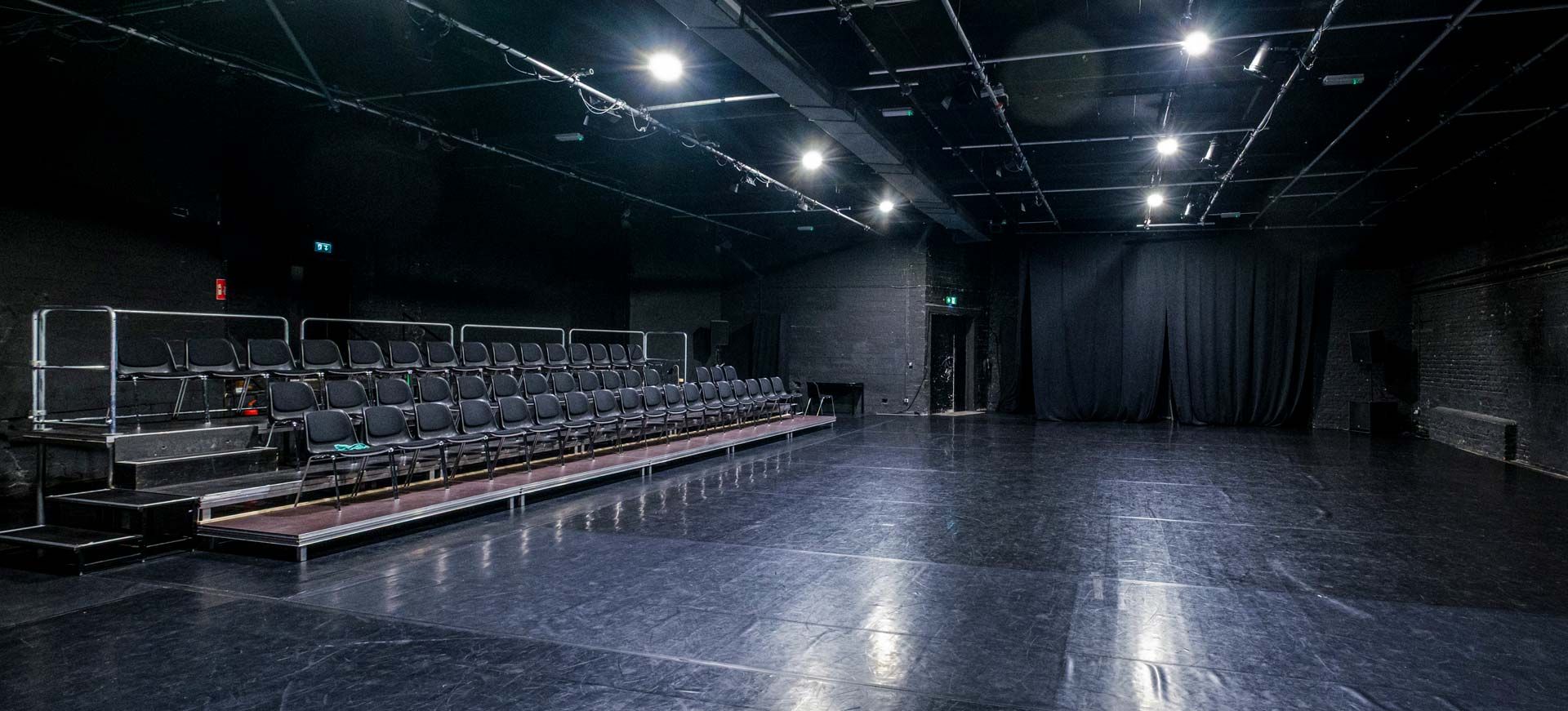Studio 1 / Black Box bei Barnes Crossing mit schwarzem Tanzboden, Zuschauertribüne, Stuhlreihen (links) und Bühnentechnik.