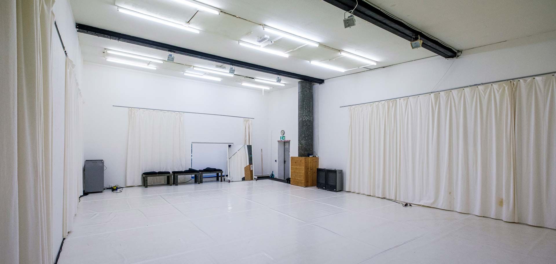 Studio 2 / White Cube bei Barnes Crossing mit hellem Tanzboden, weißen Wänden, teilweise abgehängt mit weißen Vorhängen, und Bänken an einer Wand.